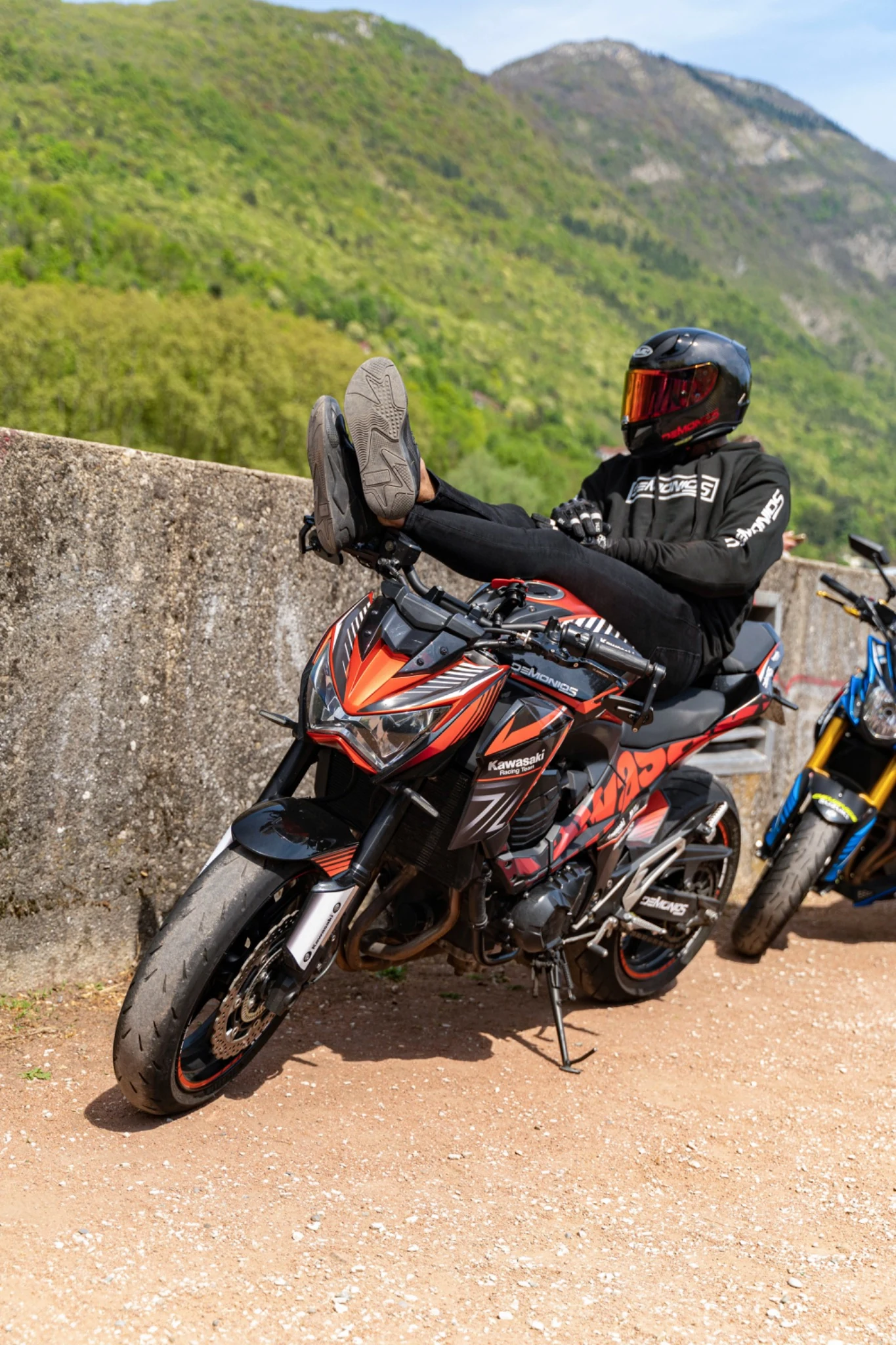 Pause lors d’une balade à moto : motard assis sur une Kawasaki orange et noire devant un paysage de montagne.